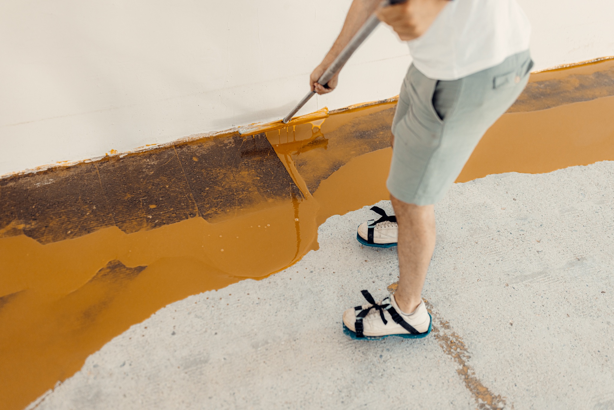 Handyman applies yellow liquid paint on new floor